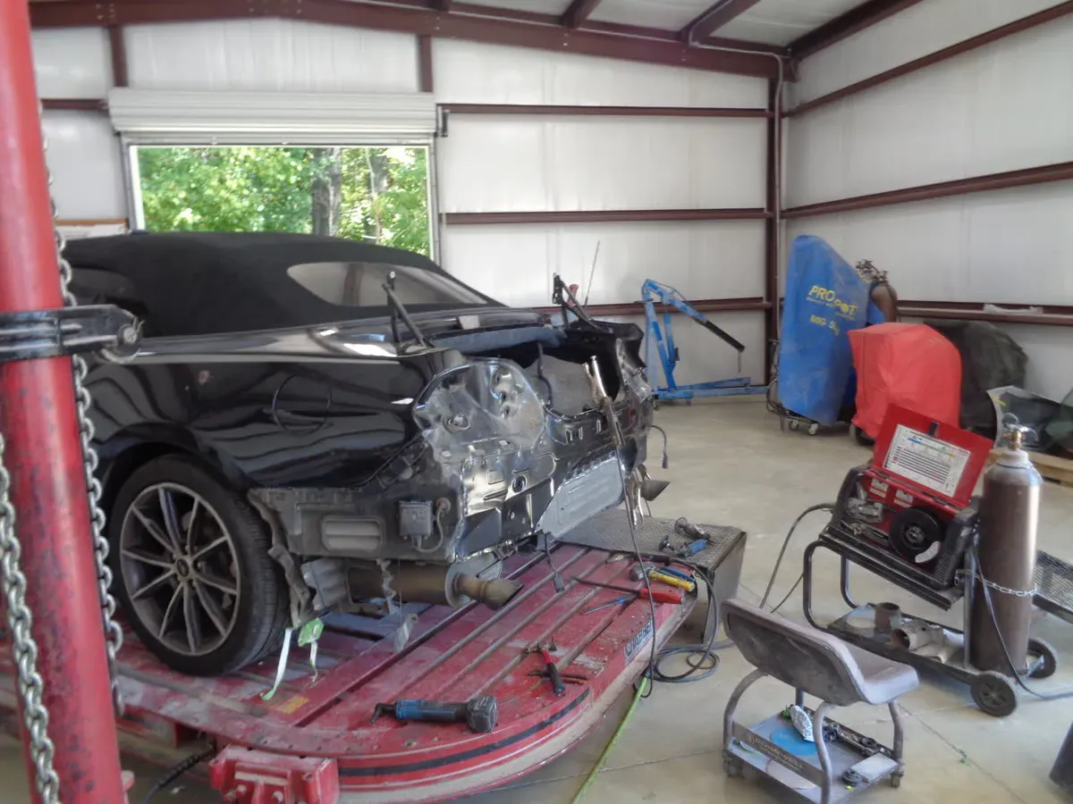 Black convertible with rear collision damage chained to a frame straightening machine in the shop